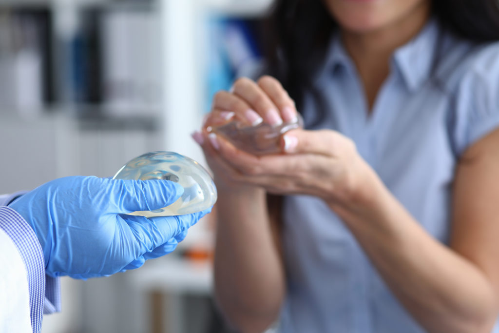 breast implant selection. CDoctor's hands in gloves holding breast implant. Young woman is holding female breast silicone implant in her hands.