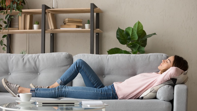 Tired young woman lying on cozy couch take nap daydreaming in living room, peaceful girl relax on comfortable sofa with eyes closed sleeping resting at home, female feel fatigue fall asleep